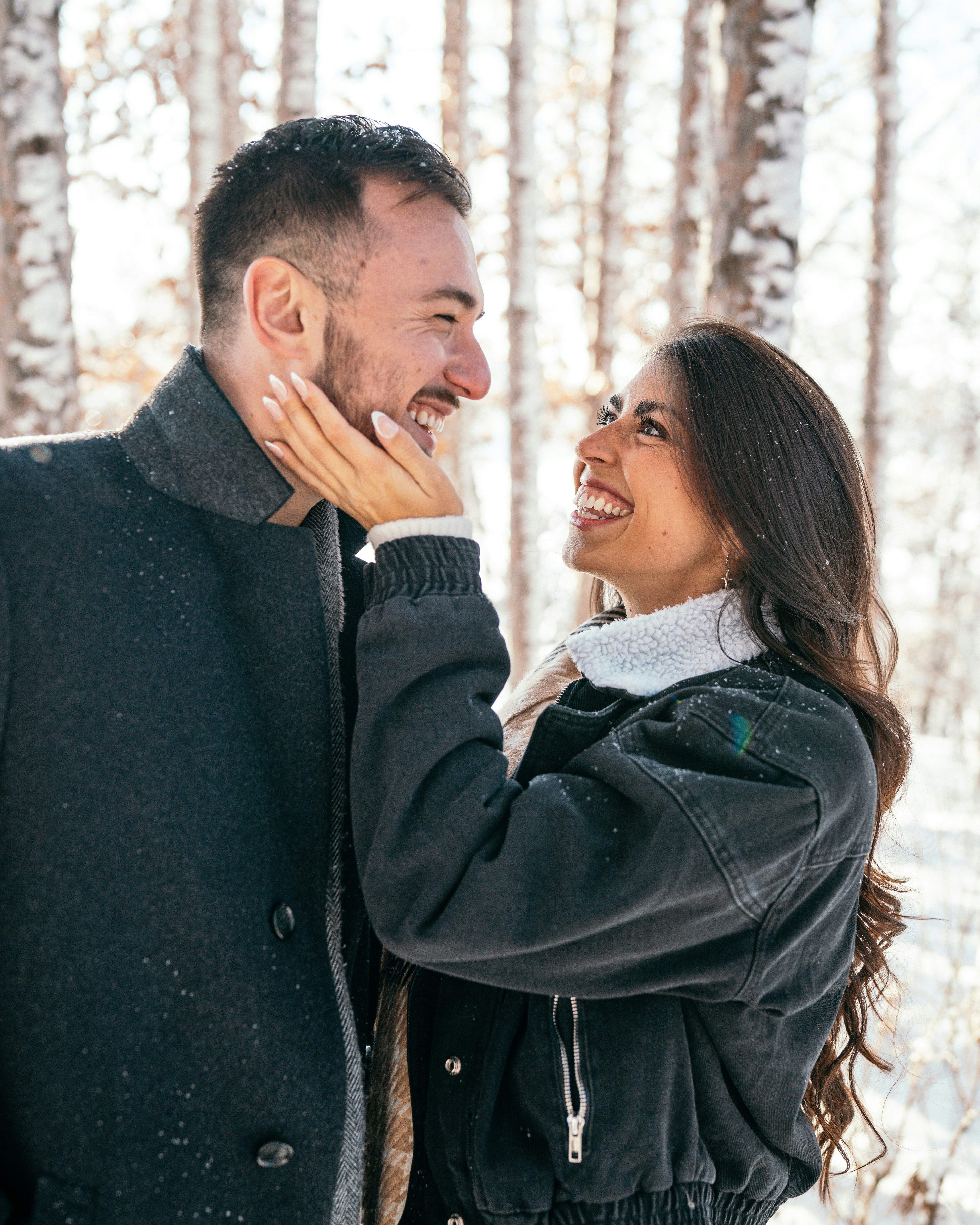Happy couple smiling at each other in a snowy birch forest.