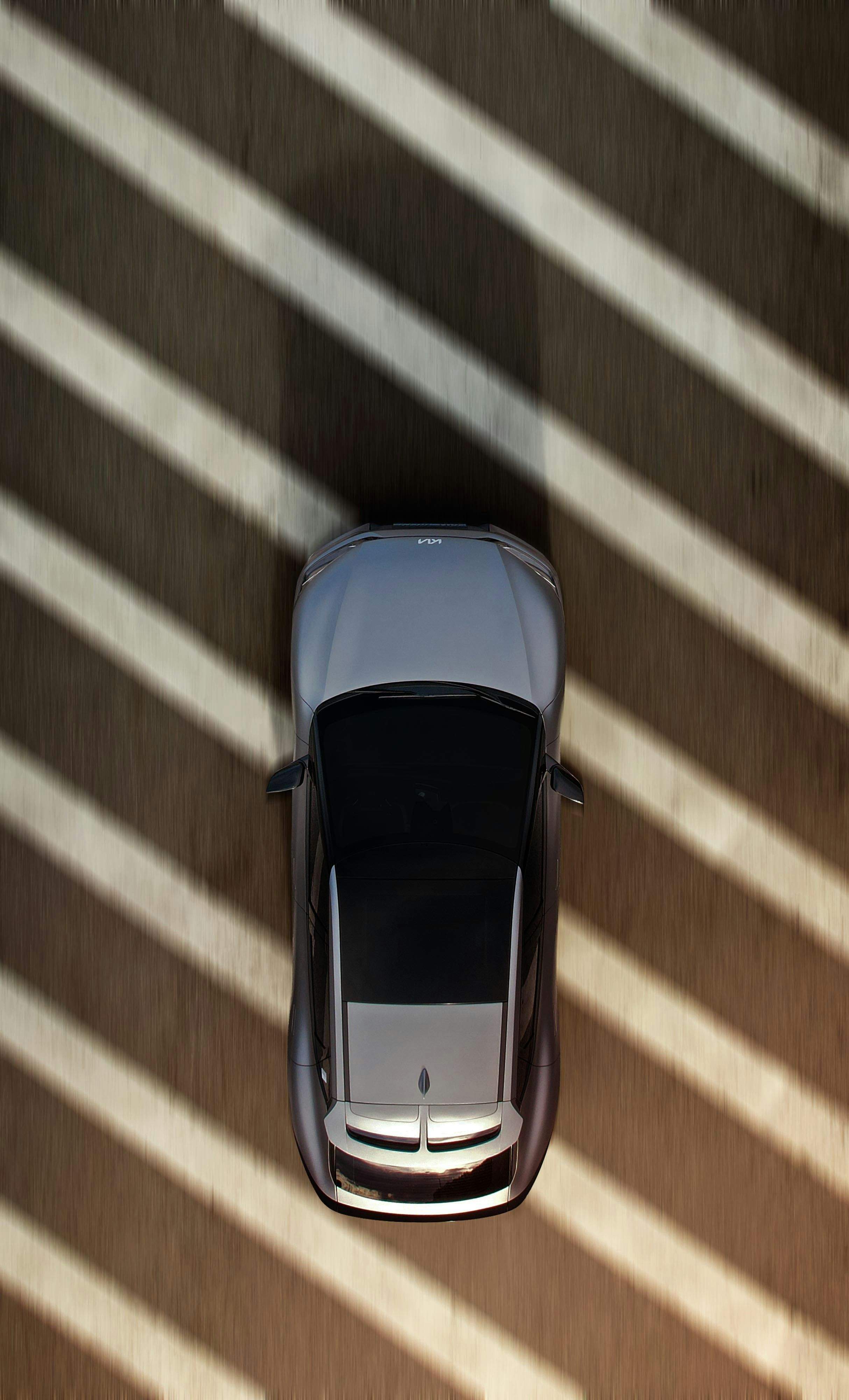 A light-colored car is seen from above, parked on a striped crosswalk.