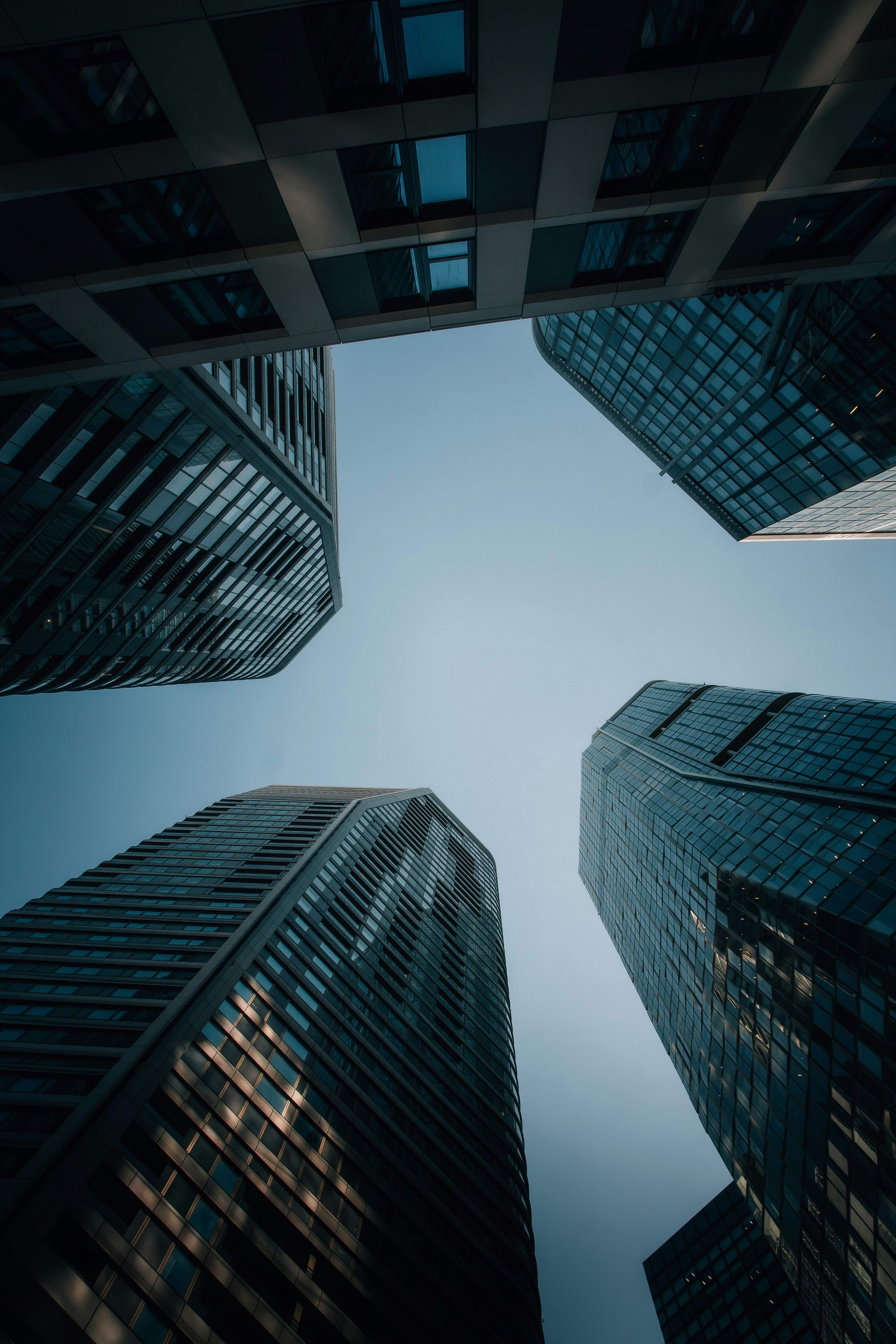 Four modern glass skyscrapers reaching skyward, viewed from below against a clear blue sky.