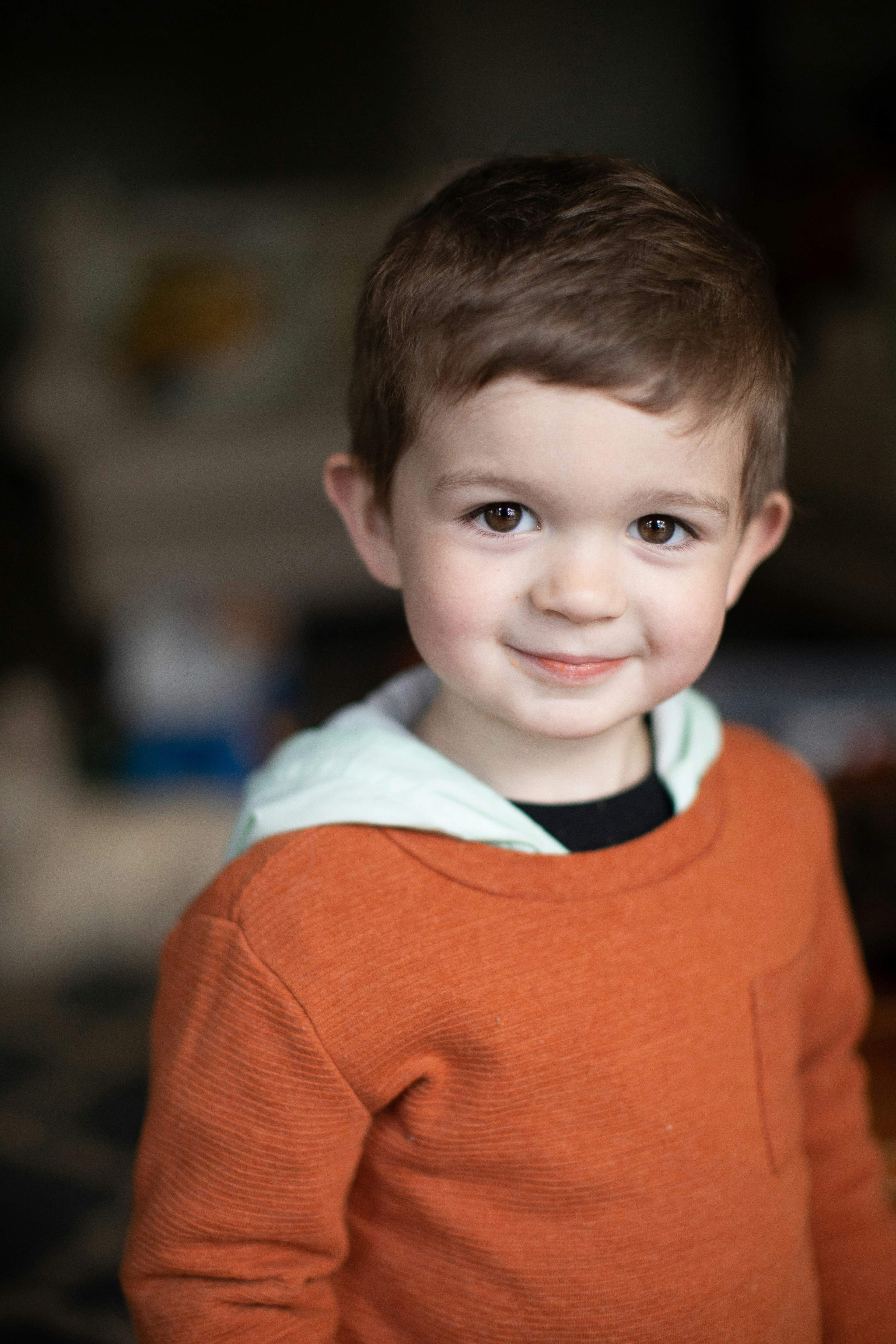 Smiling young boy with brown hair wearing an orange shirt looking directly at the camera.