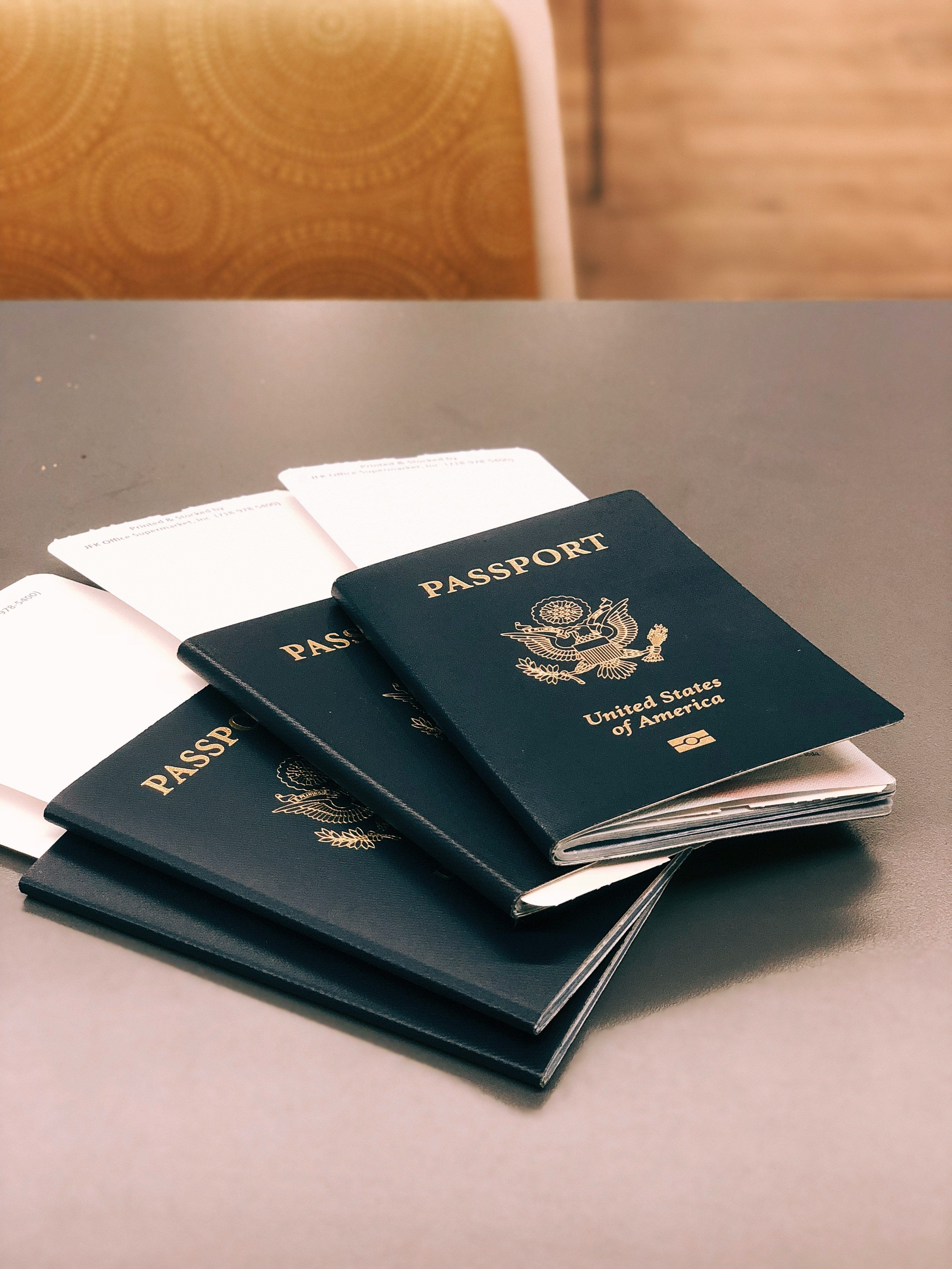Three dark blue US passports are stacked on a table with white documents underneath.