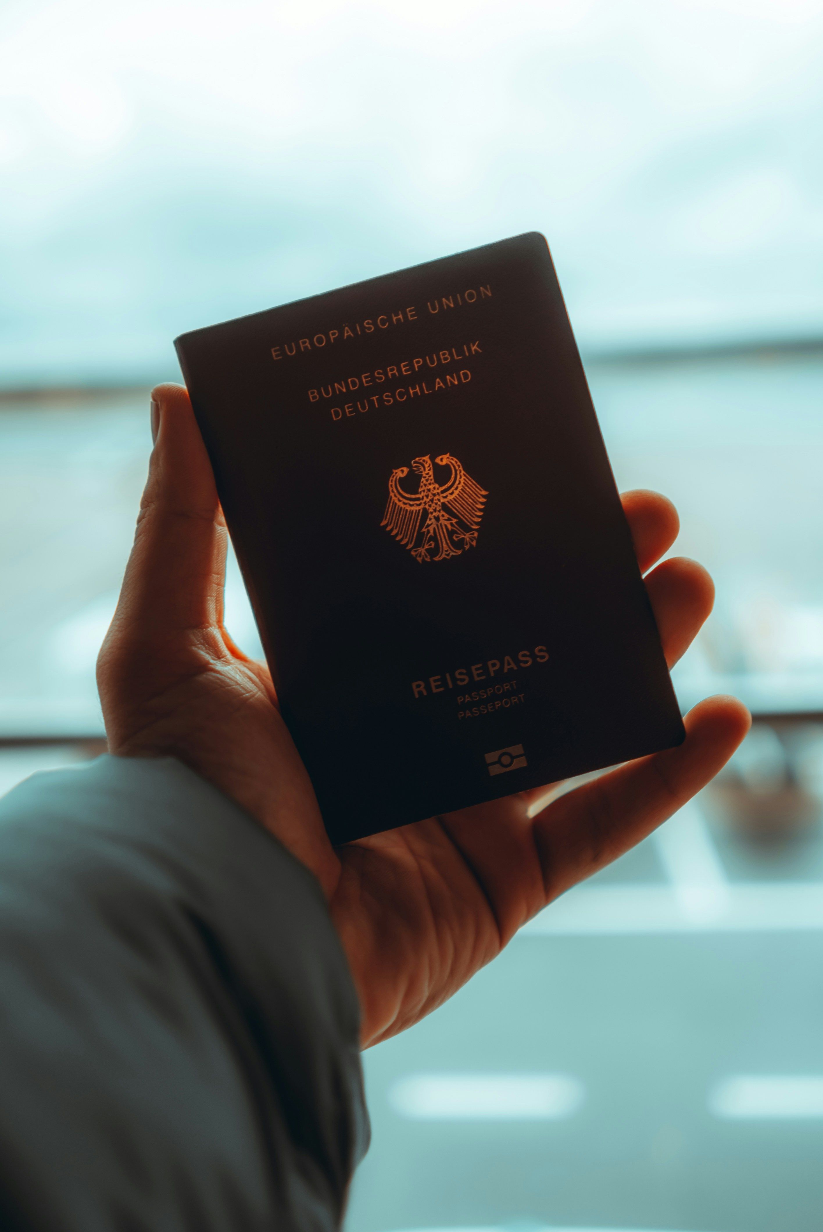 Hand holding a dark blue German passport with the eagle emblem visible.
