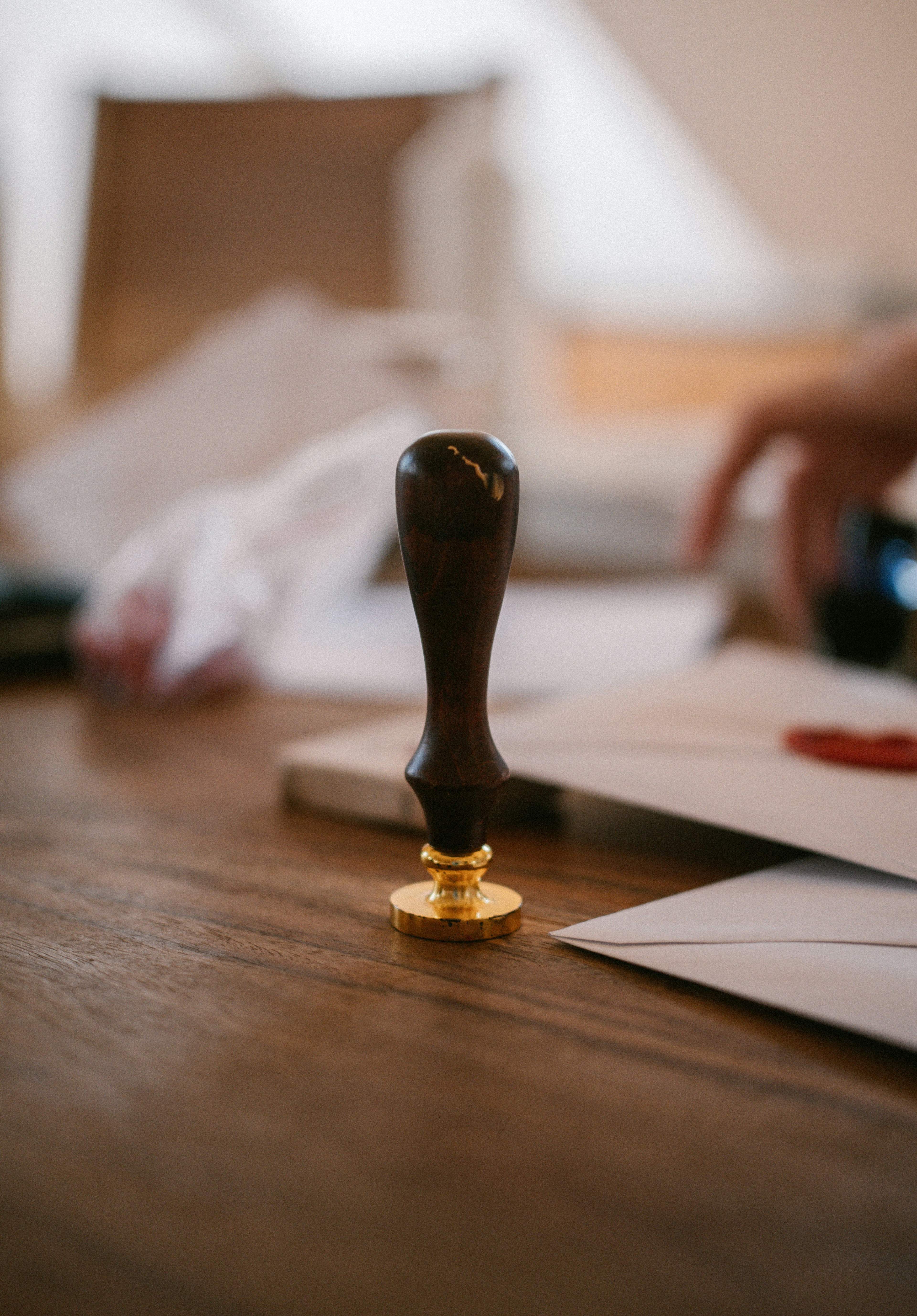 Vintage wax seal stamp with dark handle and golden base on a wooden desk.