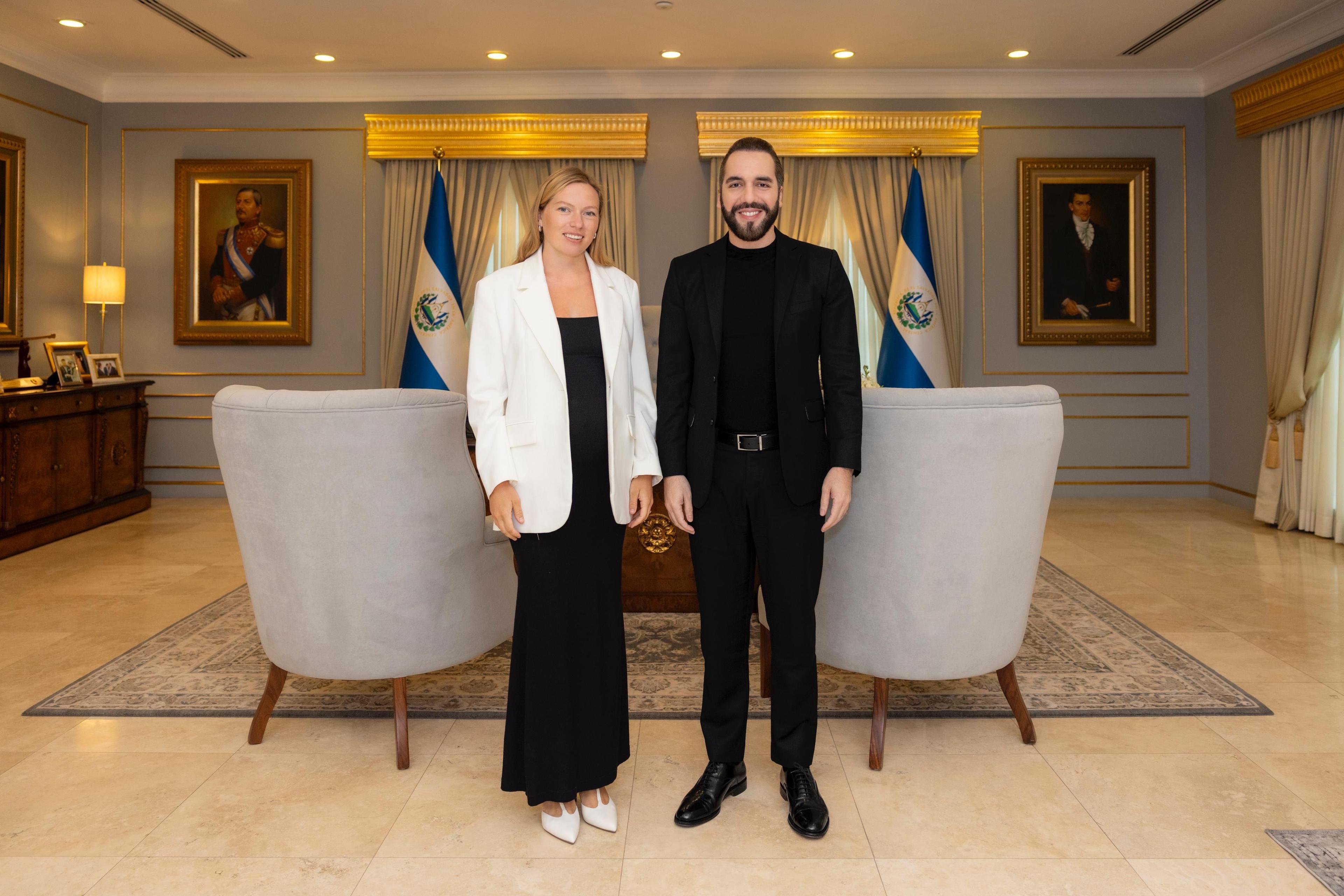 Woman in white blazer and man in black suit standing in an elegant office.