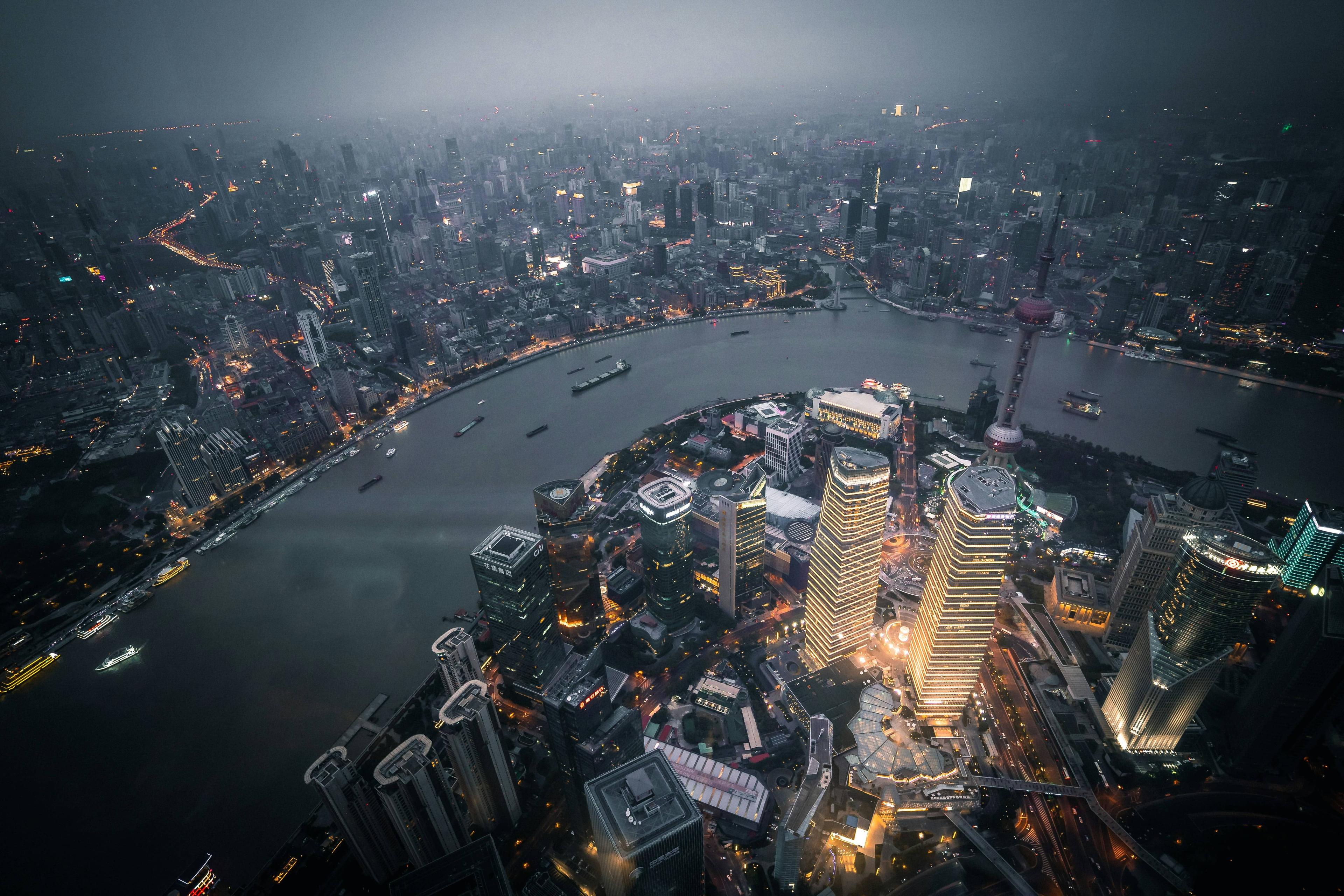 Aerial view of a bustling city at night, with illuminated skyscrapers along a wide river.