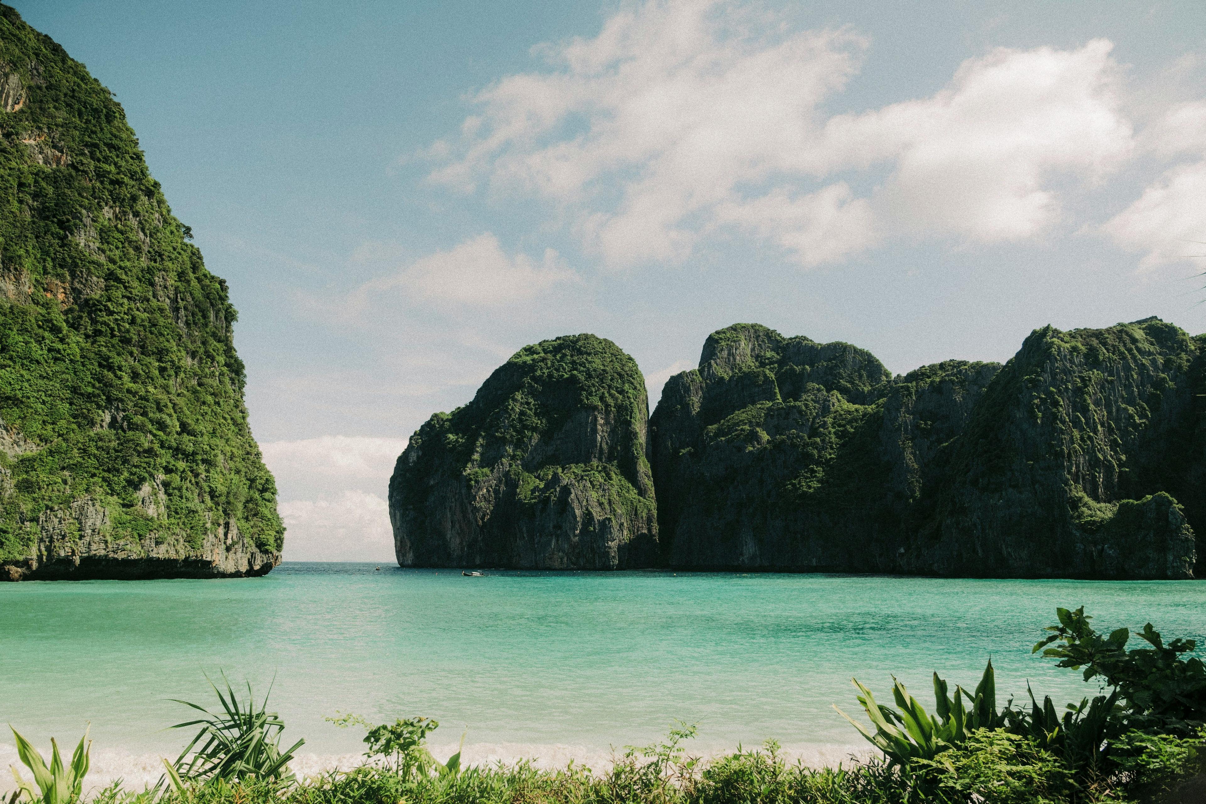 Turquoise ocean with towering green cliffs, sandy beach, and clear blue sky.