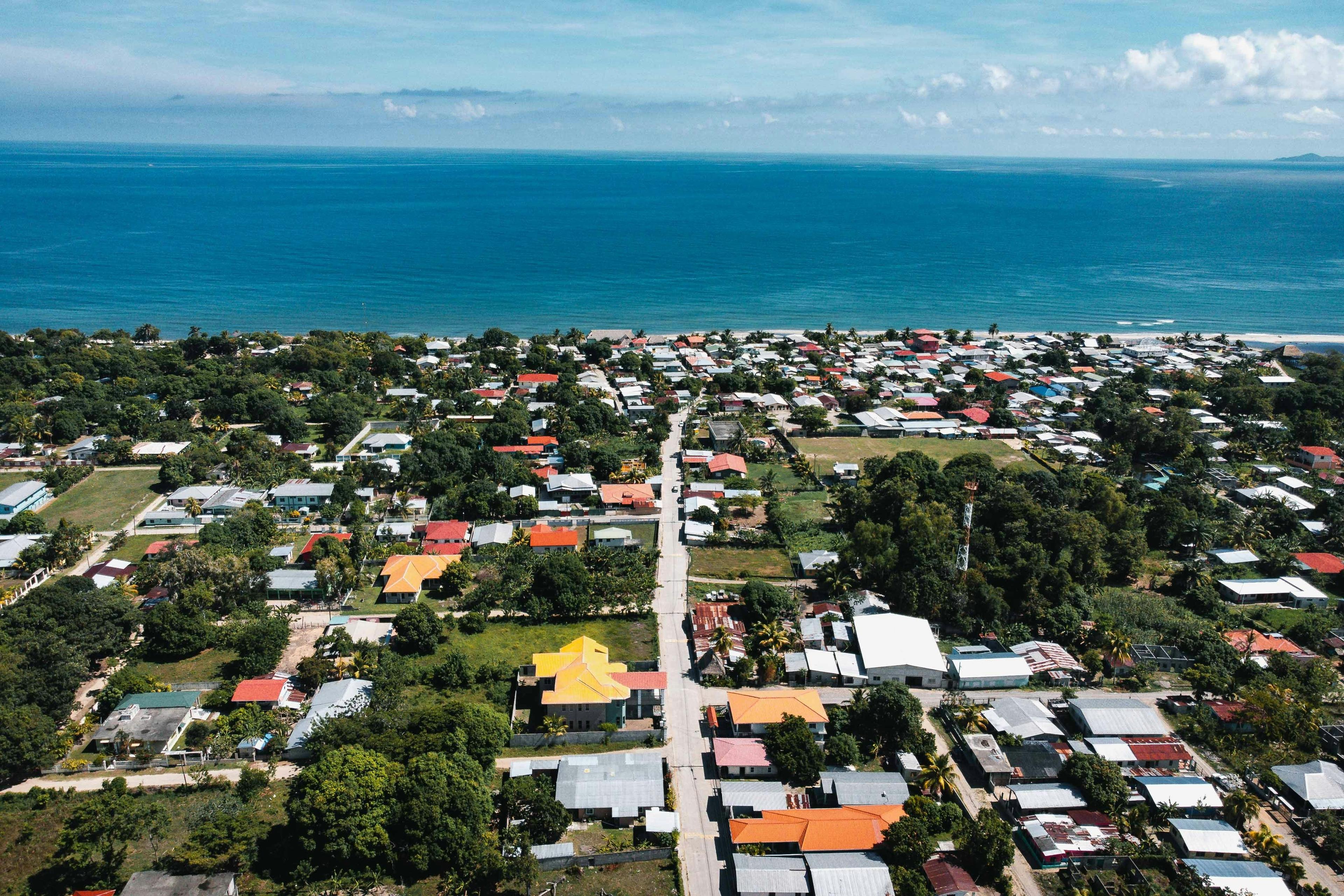 Aerial view of a coastal town showing colorful houses, green trees, and a blue ocean.