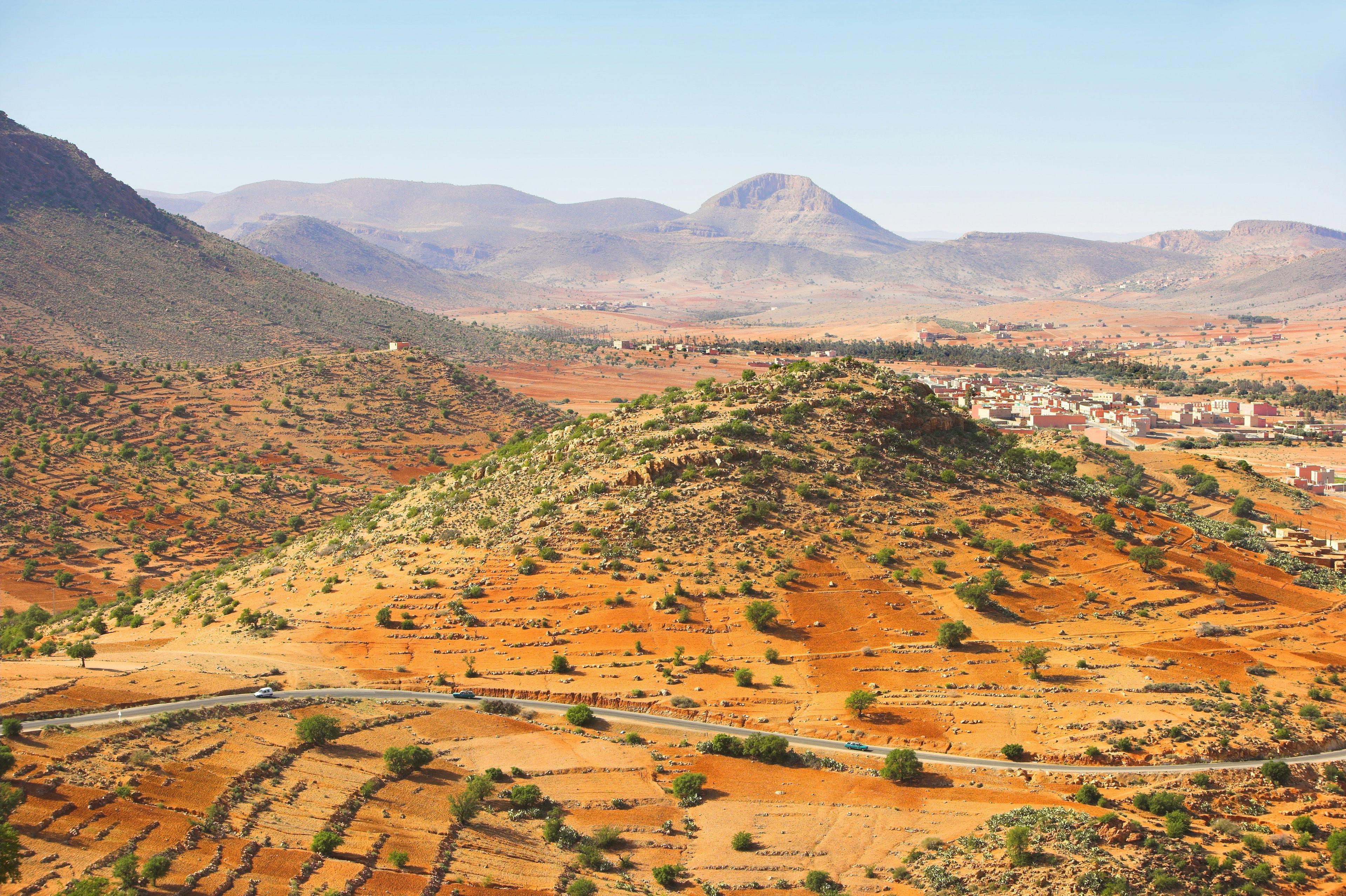Arid landscape with green hills, terraced fields, and a distant village under a clear sky.