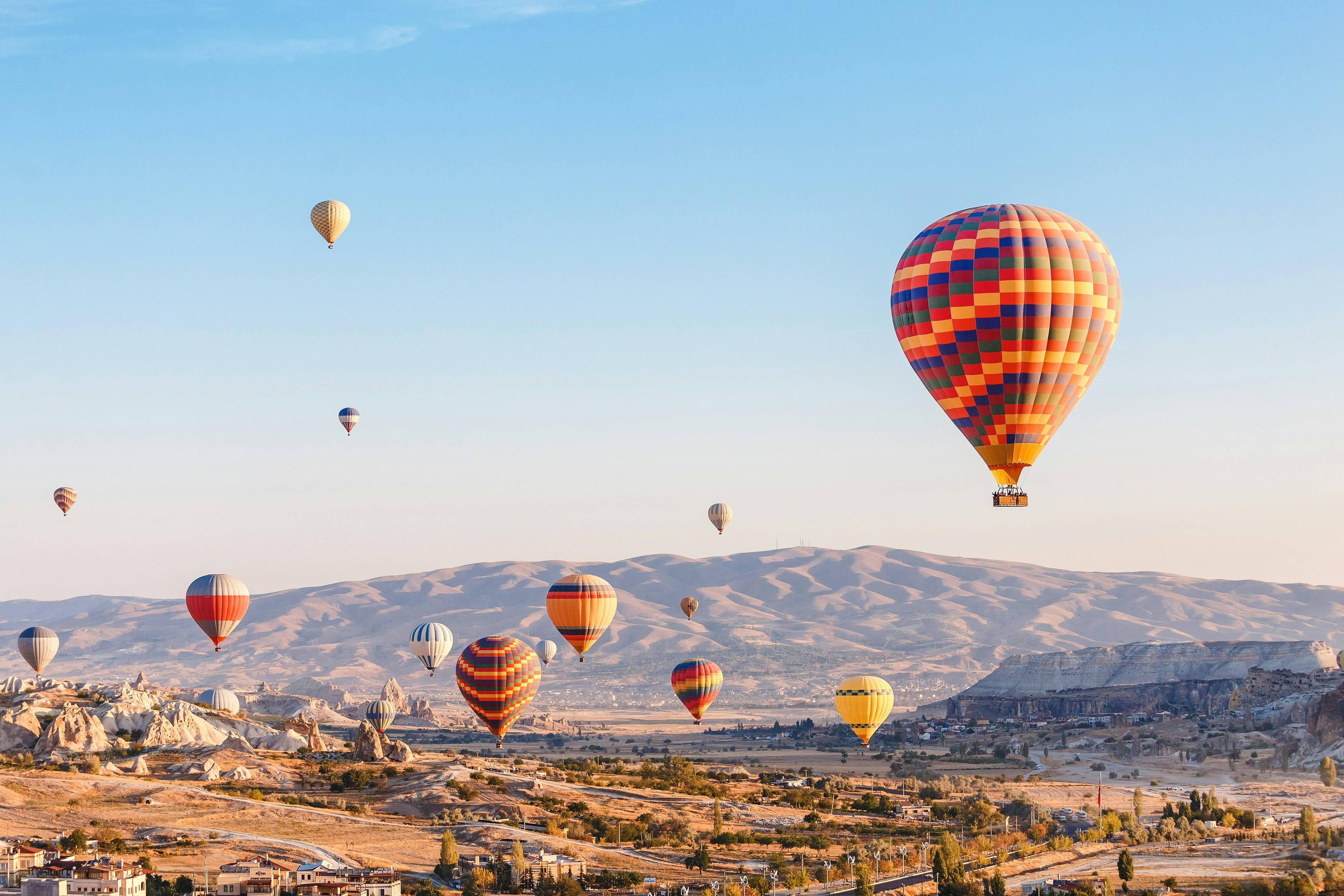 Numerous colorful hot air balloons float peacefully over a mountainous landscape with a clear sky.