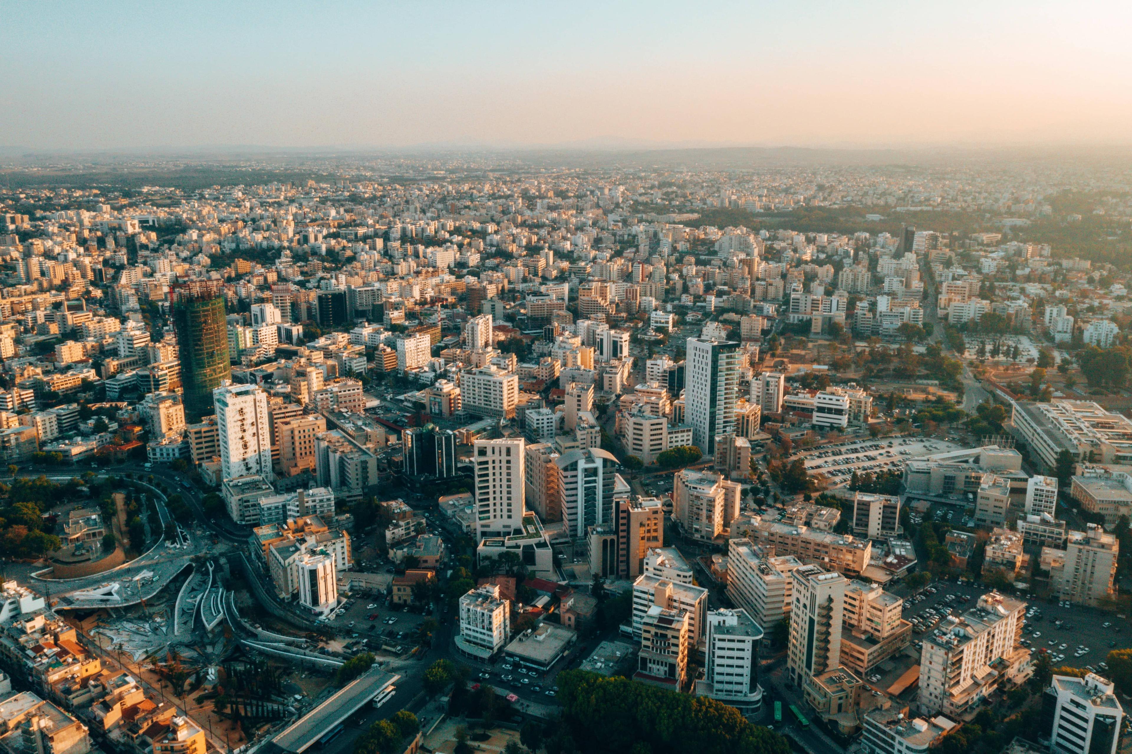 Aerial view of a vast modern city with numerous buildings under a clear, warm sky.