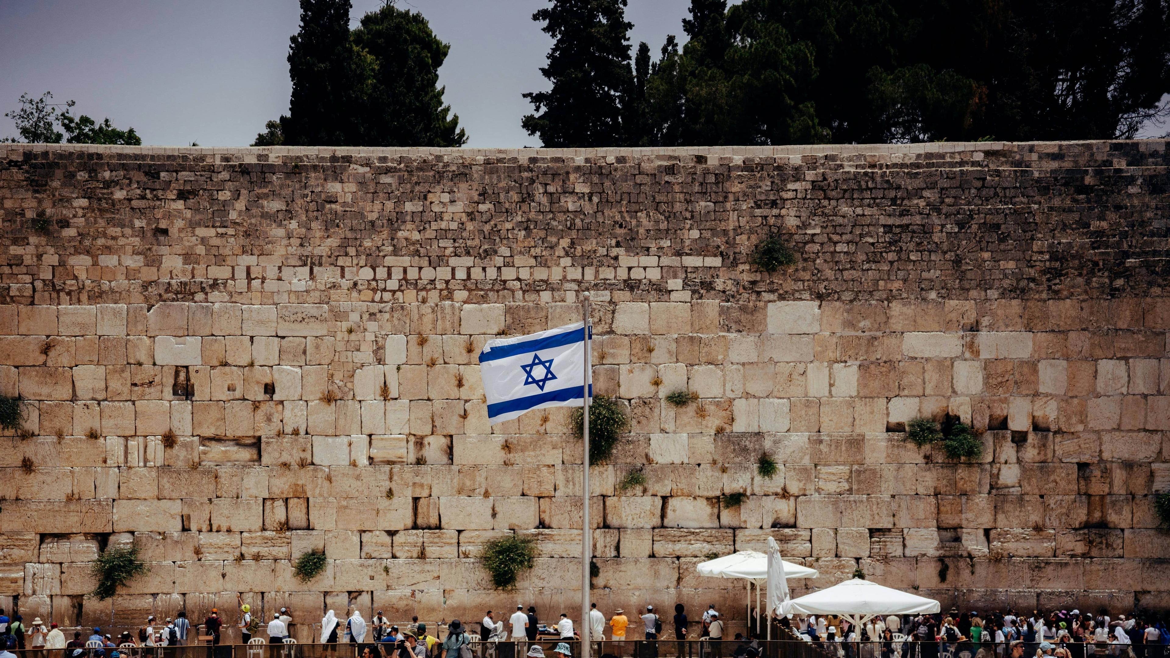 Israeli flag waves proudly against the ancient stone blocks of Jerusalem's Western Wall.