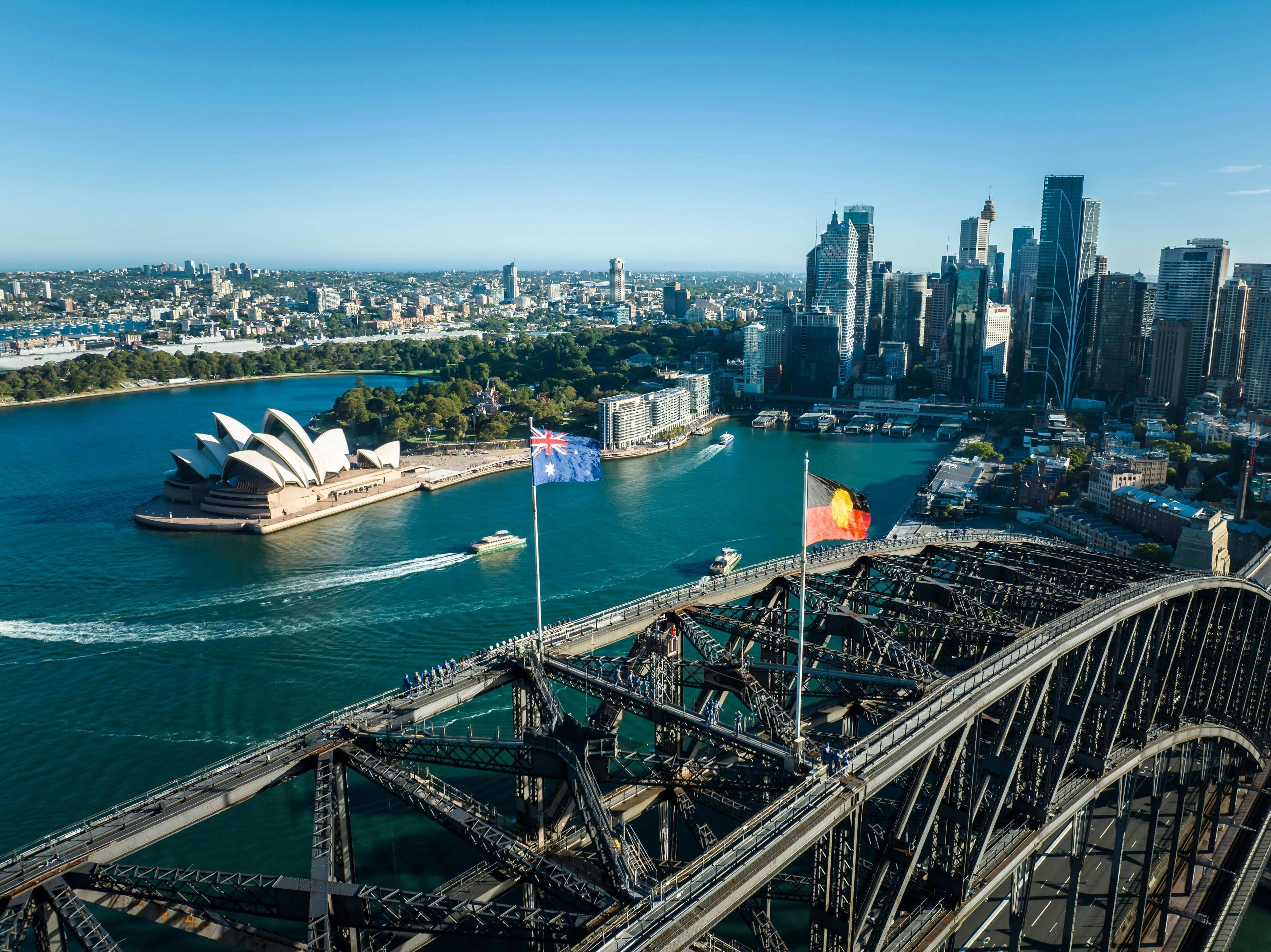Sydney Harbour with Opera House, Harbour Bridge, and city skyline under clear sky.
