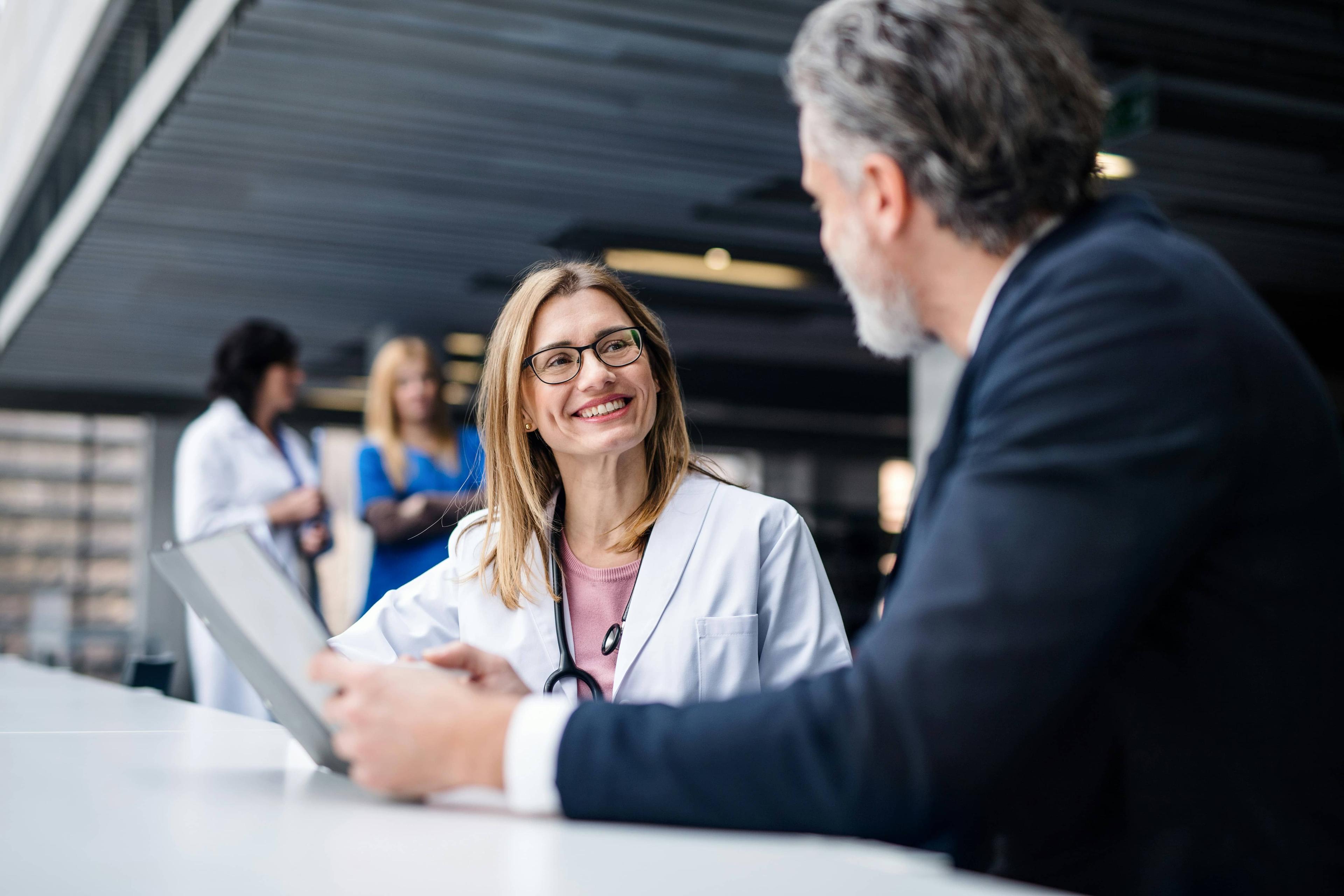 Female doctor smiling at male patient while discussing information on a tablet.