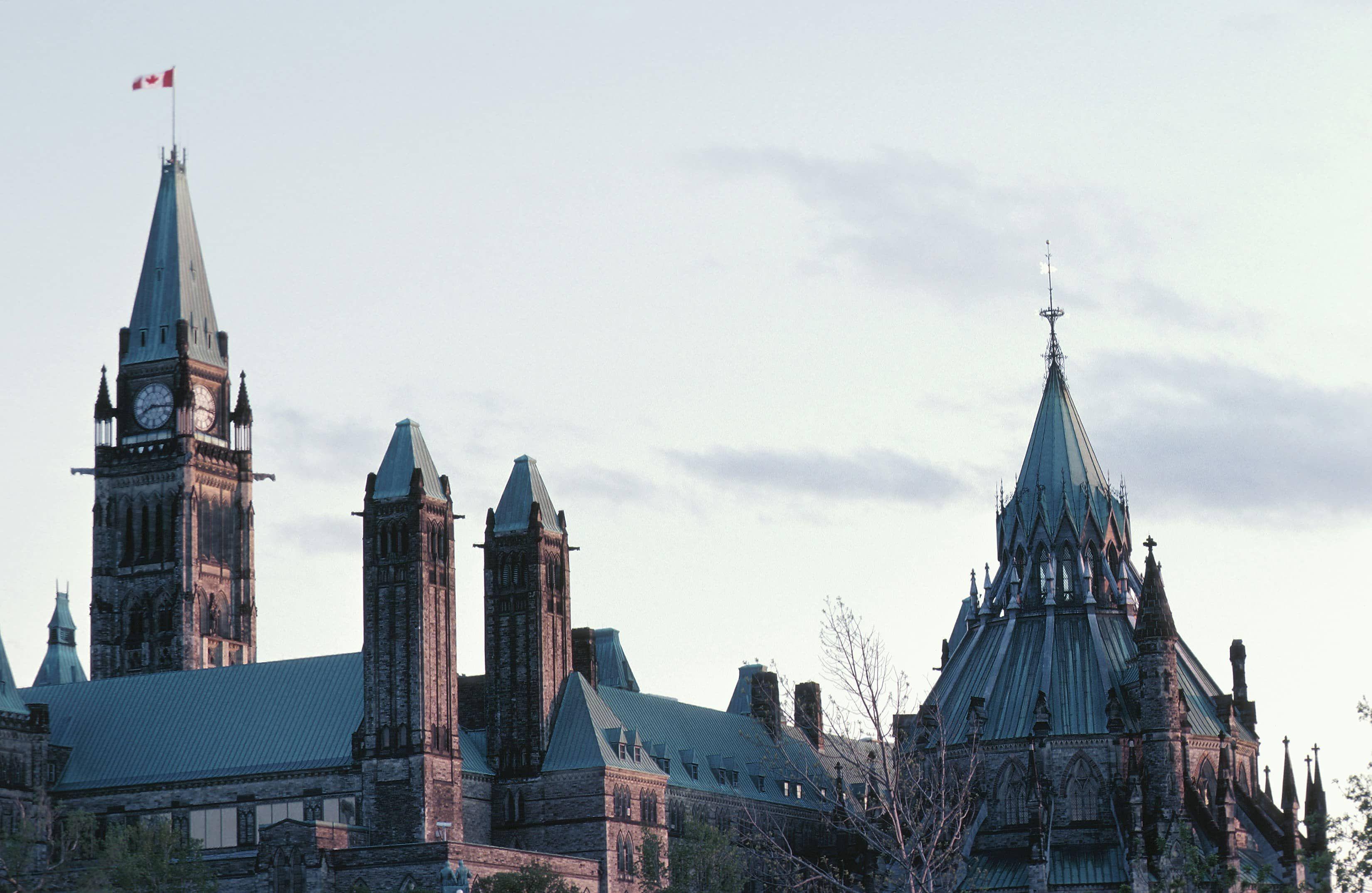 Historic Canadian Parliament building with its iconic clock tower and a Canadian flag.