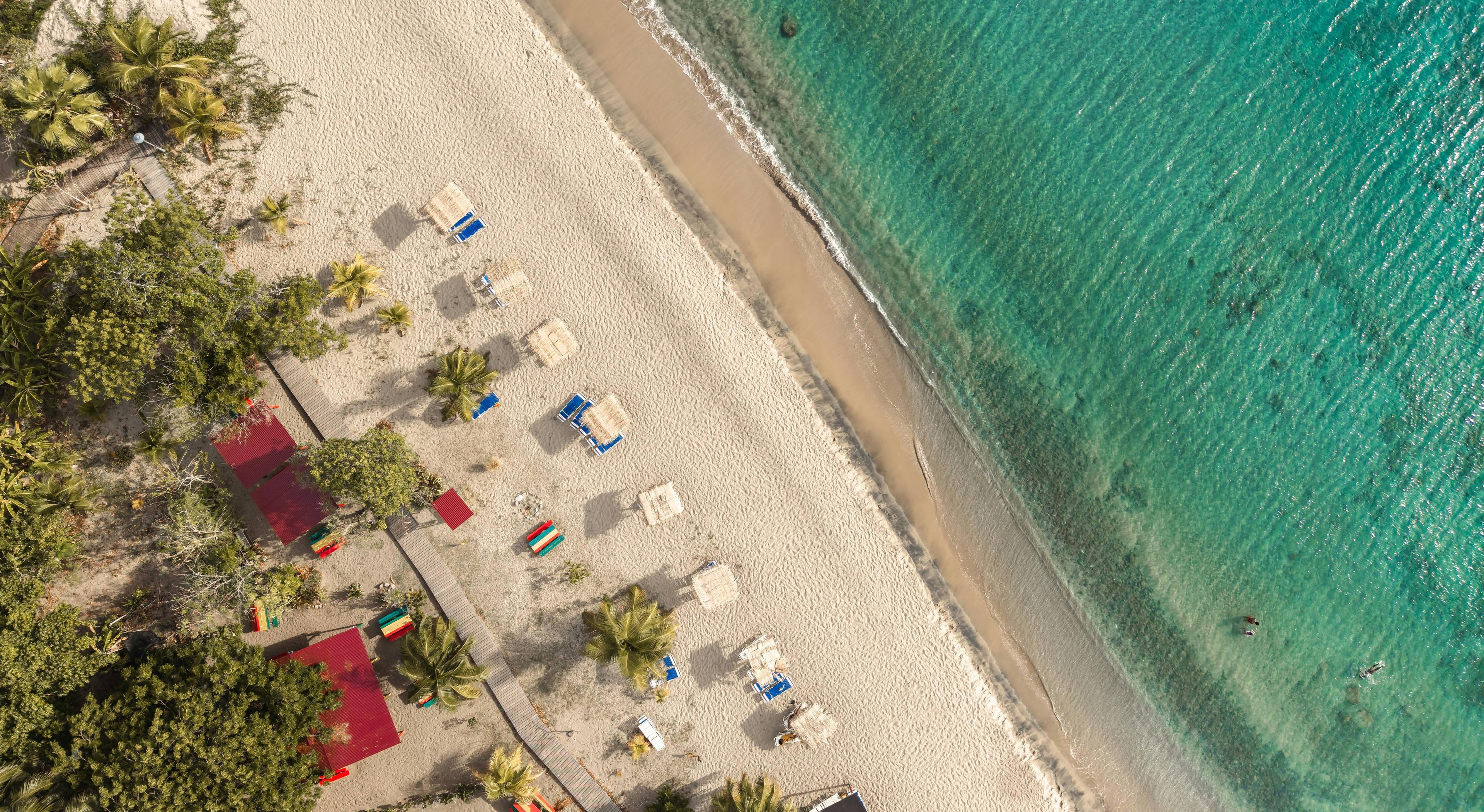 Aerial view of a tropical beach with turquoise water, white sand, and palm trees.