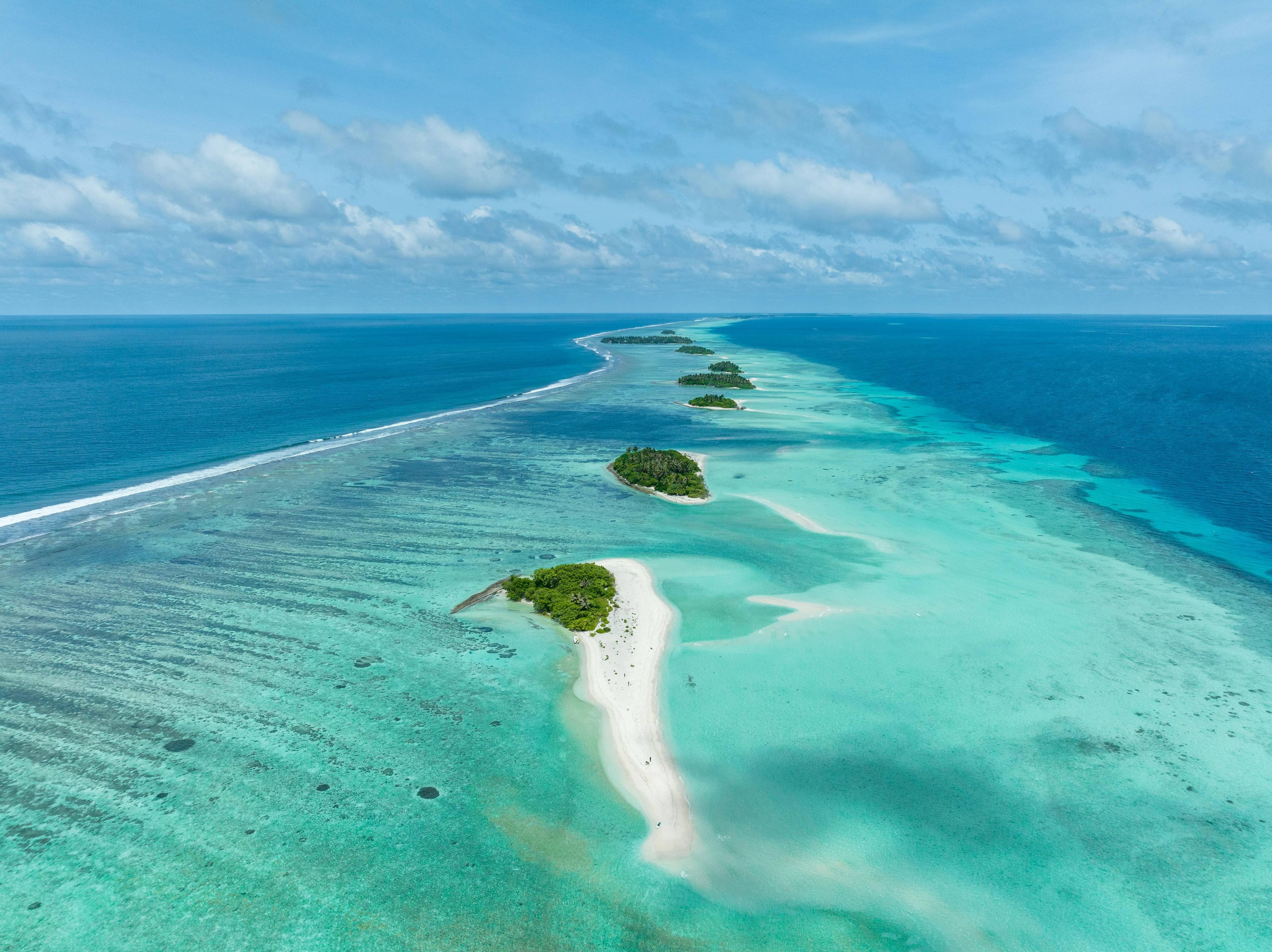 Aerial view of small tropical islands connected by a narrow sandbank in turquoise ocean.