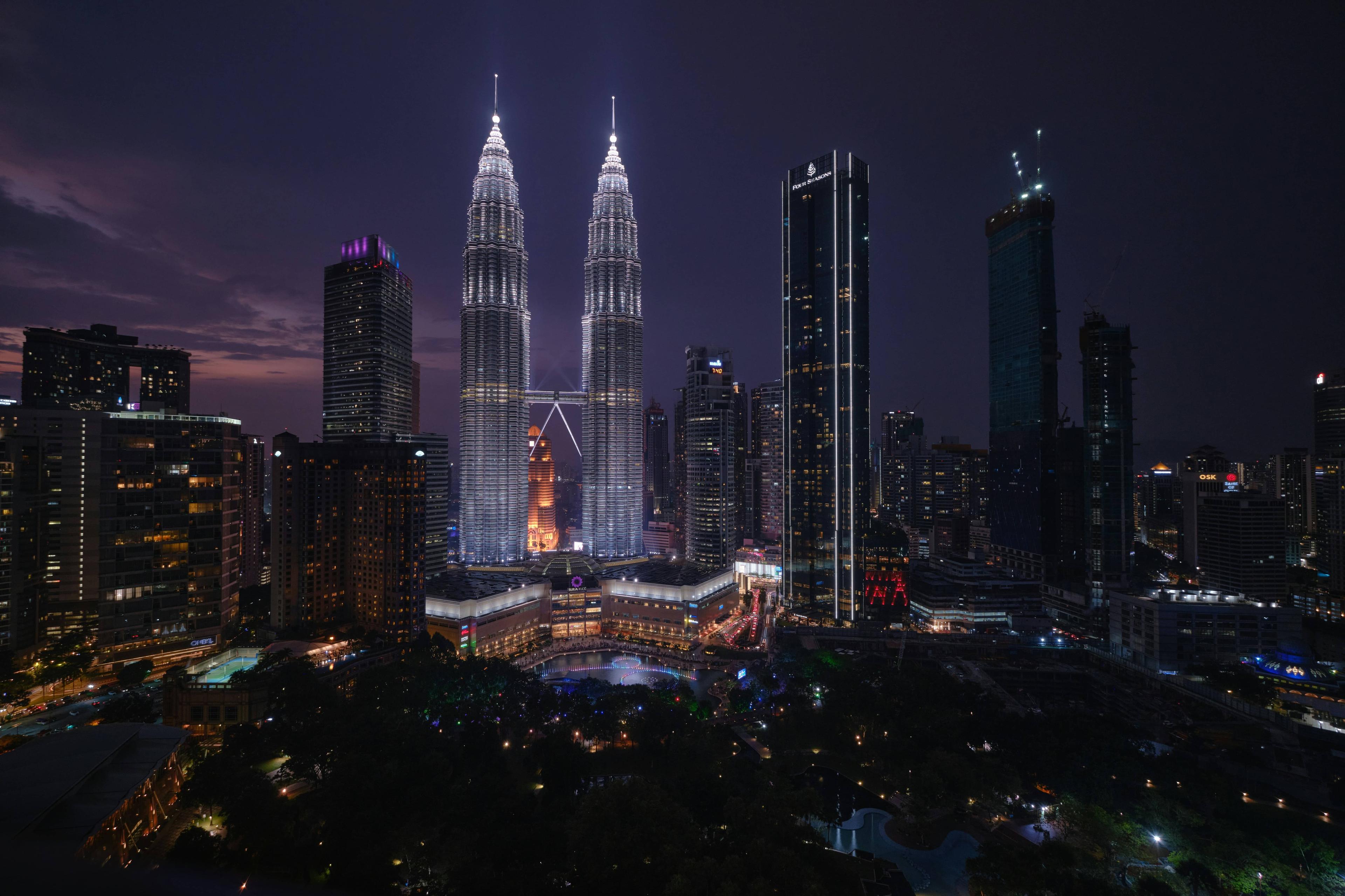 Kuala Lumpur skyline at dusk featuring the iconic, brightly lit Petronas Twin Towers.