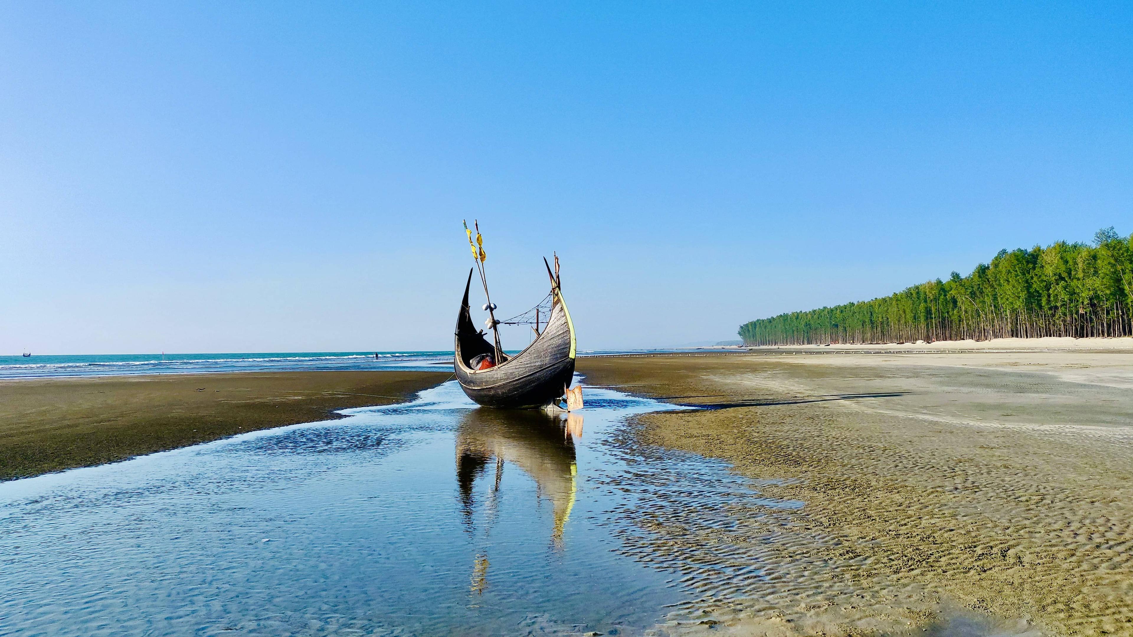 Traditional wooden boat resting on a wet sandy beach under a clear blue sky.
